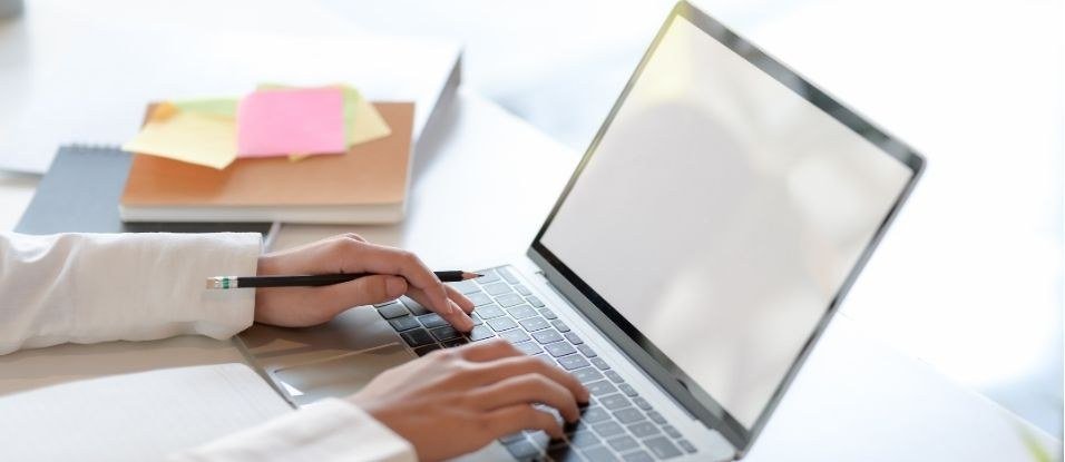 Hands typing on a laptop beside notebooks and sticky notes
